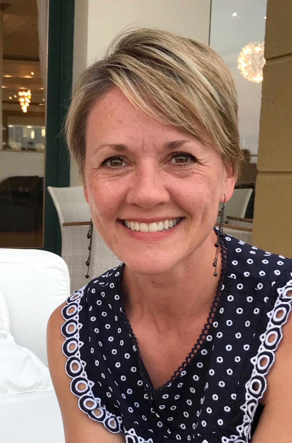 Woman with short blonde hair wearing a blue polka-dot top smiling at the camera